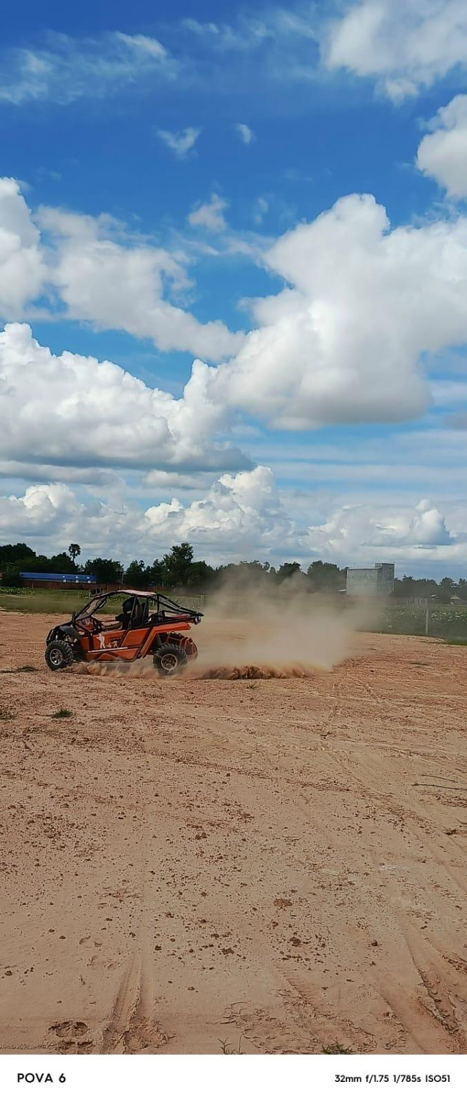 An orange off-road buggy throwing up red dust under big Cambodian clouds