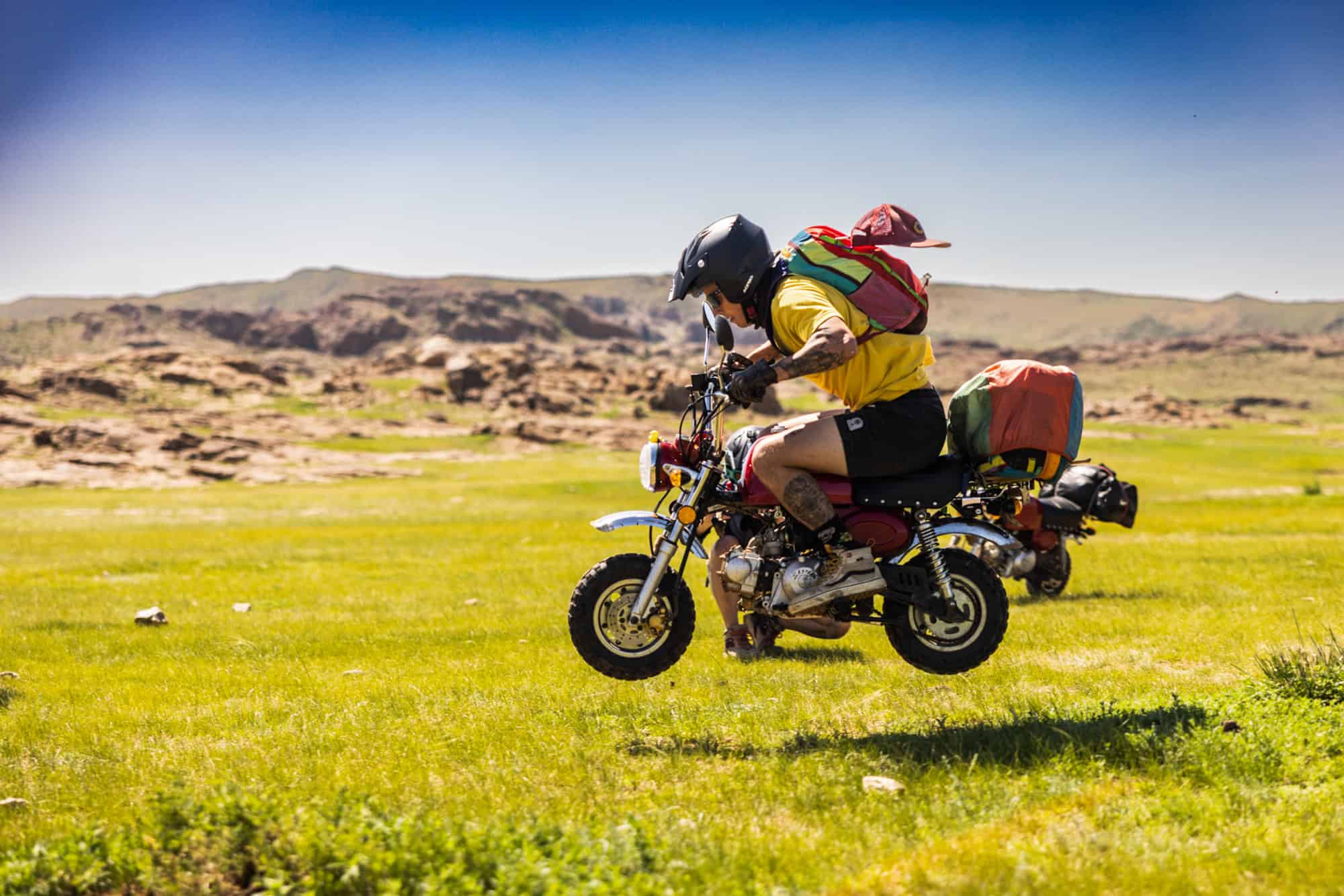 A rider on a tiny monkey bike heading down a dirt track into the open Mongolian steppe